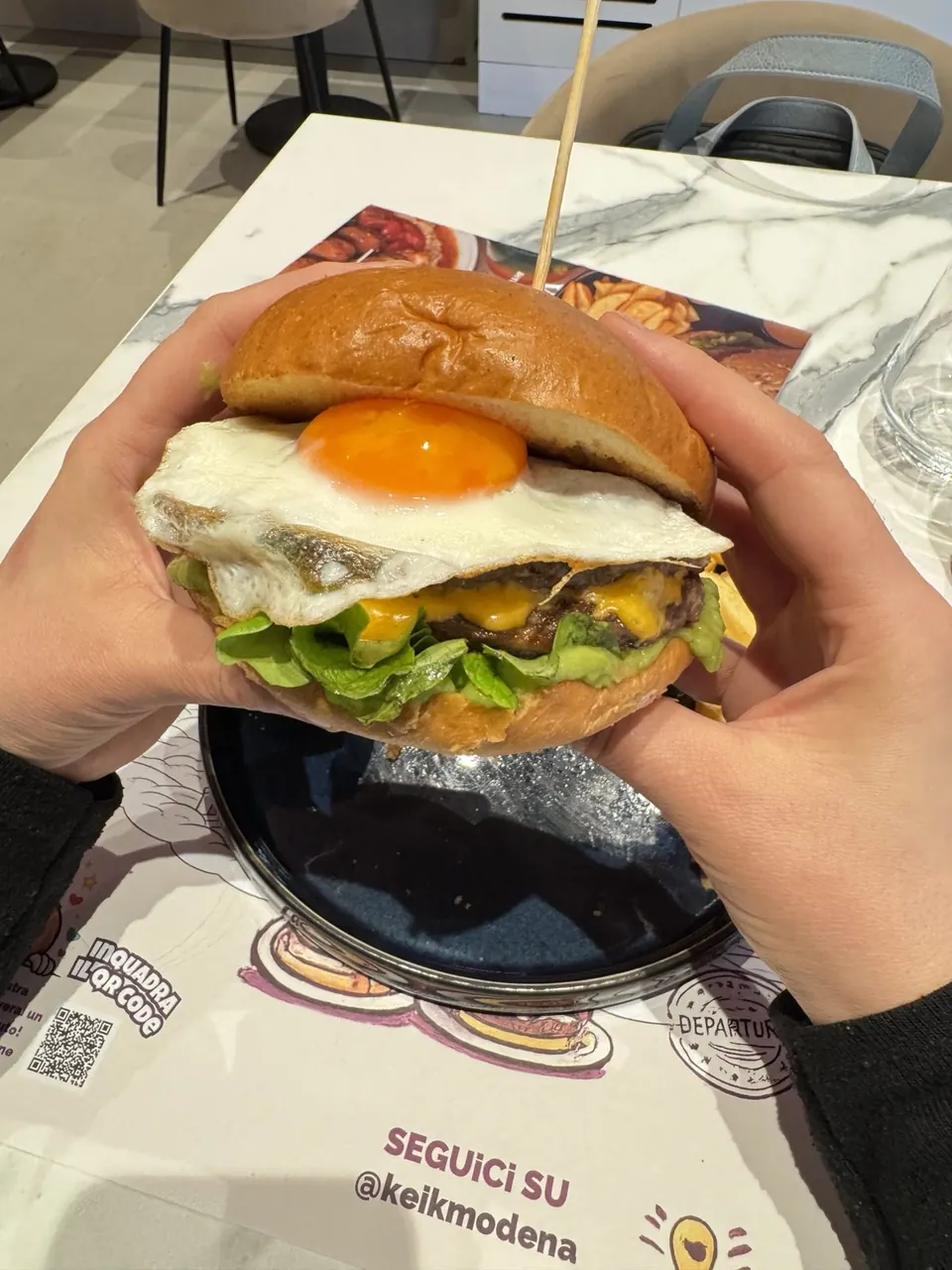 Il burger Carlitos con uovo all’occhio di bue, tenuto tra le mani