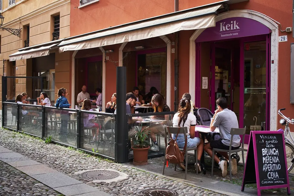Il dehors di KEIK in Via Canalino pieno di persone, con l’insegna viola e la lavagna Brunch, Merenda, Aperitivo, Cena